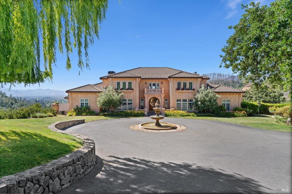 The grand front entrance of a Mediterranean-style home features a circular driveway with a central fountain. 