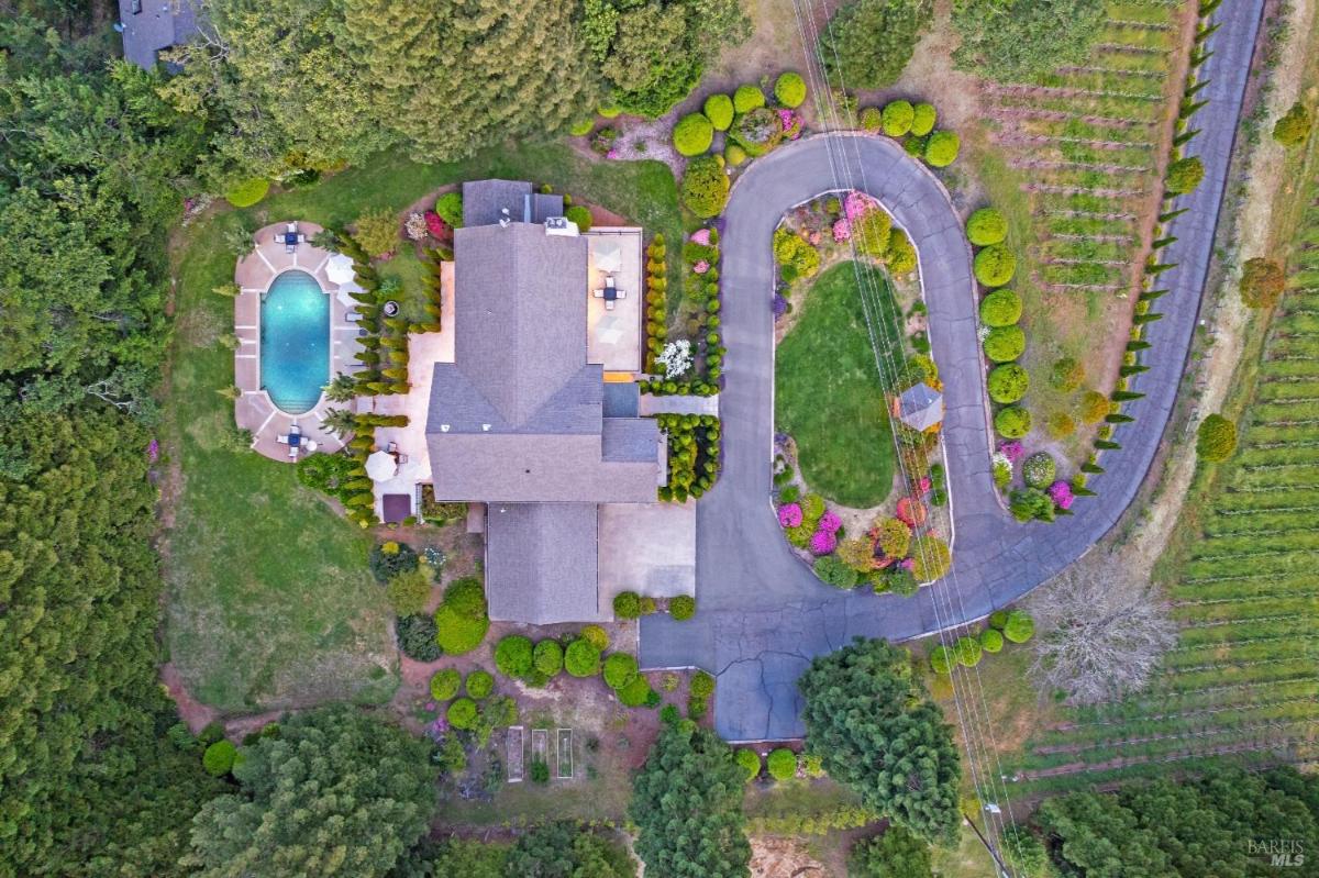 An aerial view of a spacious property featuring a house, a swimming pool, and landscaped gardens, with winding pathways and surrounding greenery. 