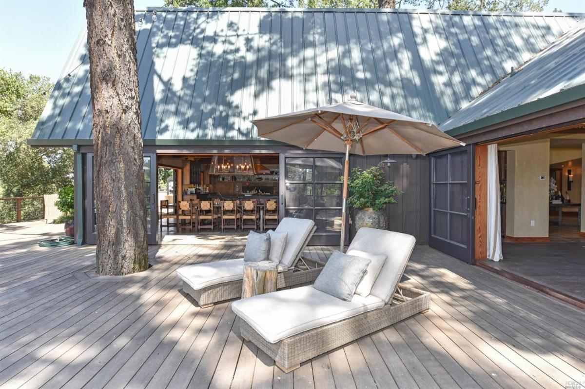 Deck with lounge chairs under an umbrella, adjacent to a building with sliding doors.