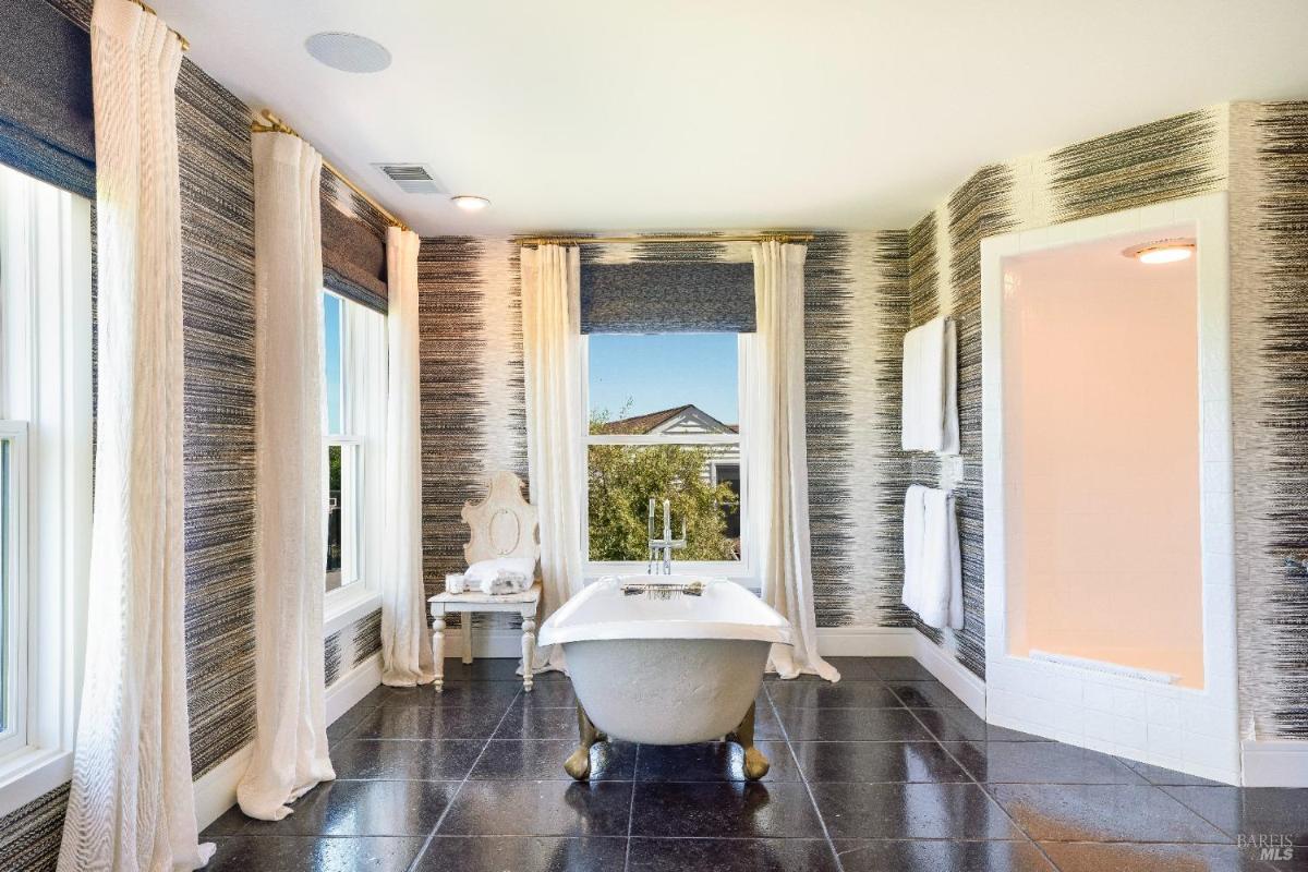 A bathroom with a standalone bathtub, large windows, and patterned walls.