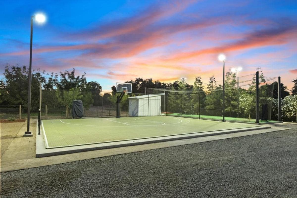 A basketball court with lights and a storage shed at sunset.