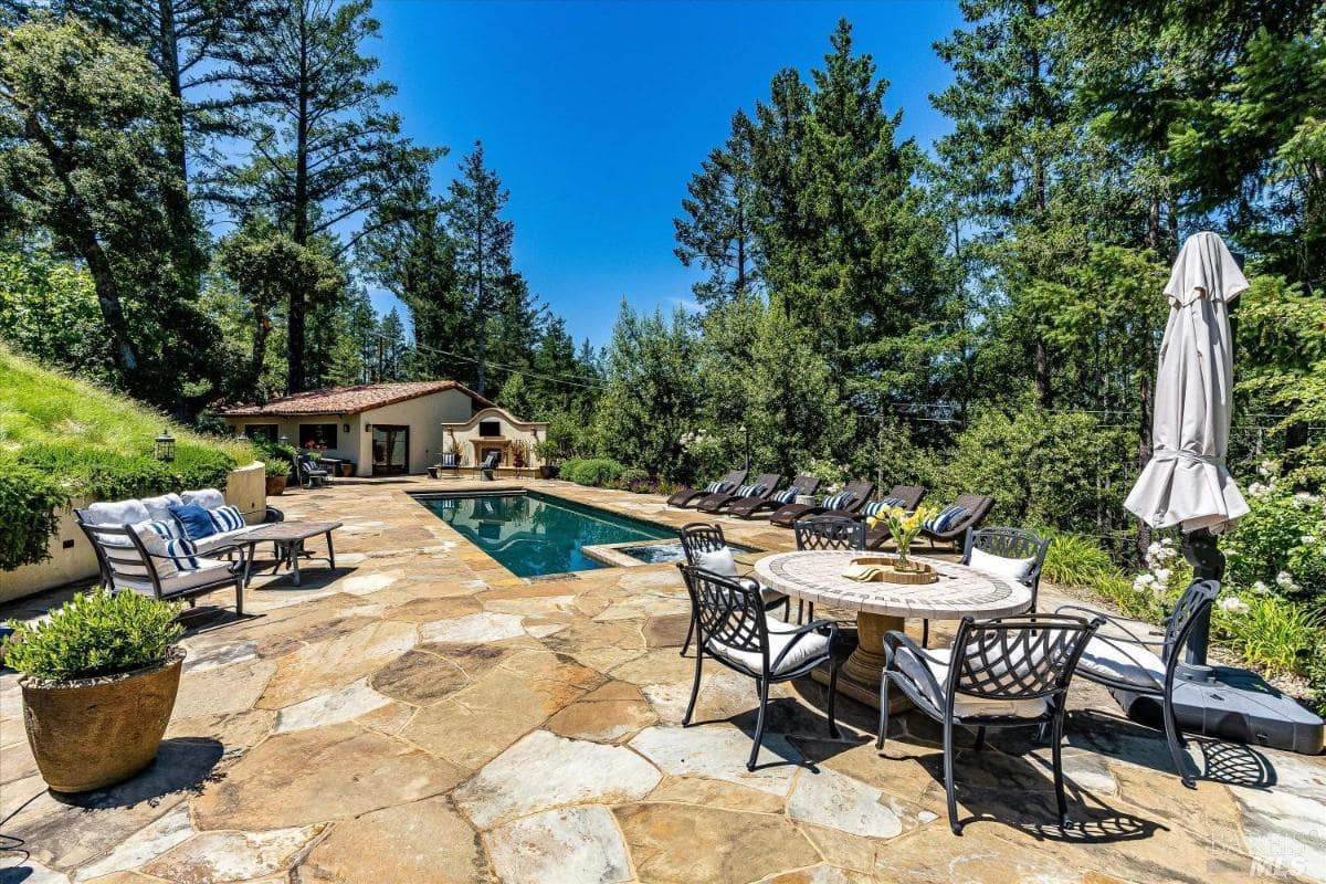 A pool area with lounge chairs, a dining table, and surrounding greenery.