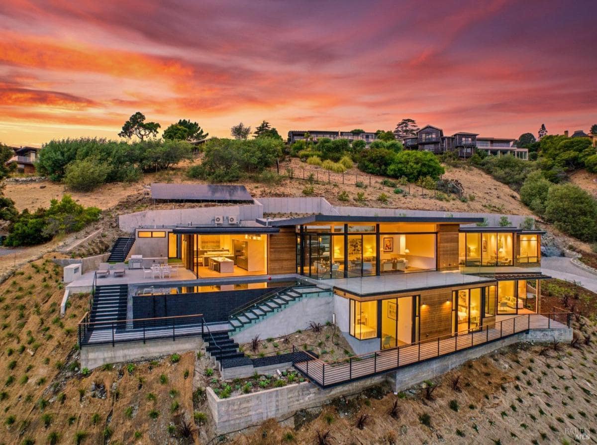 A multi-level modern home built into a hillside, with large glass windows.