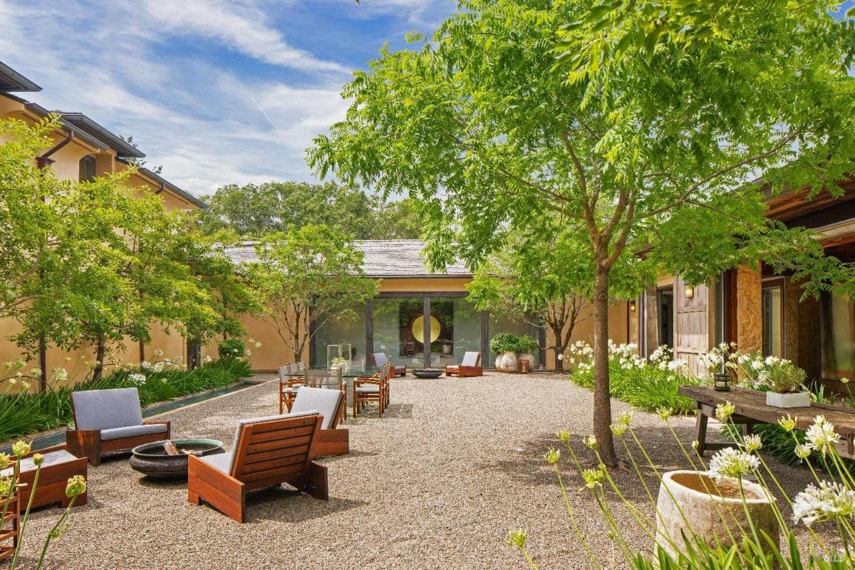 A gravel courtyard with trees, chairs, and a central fire pit.