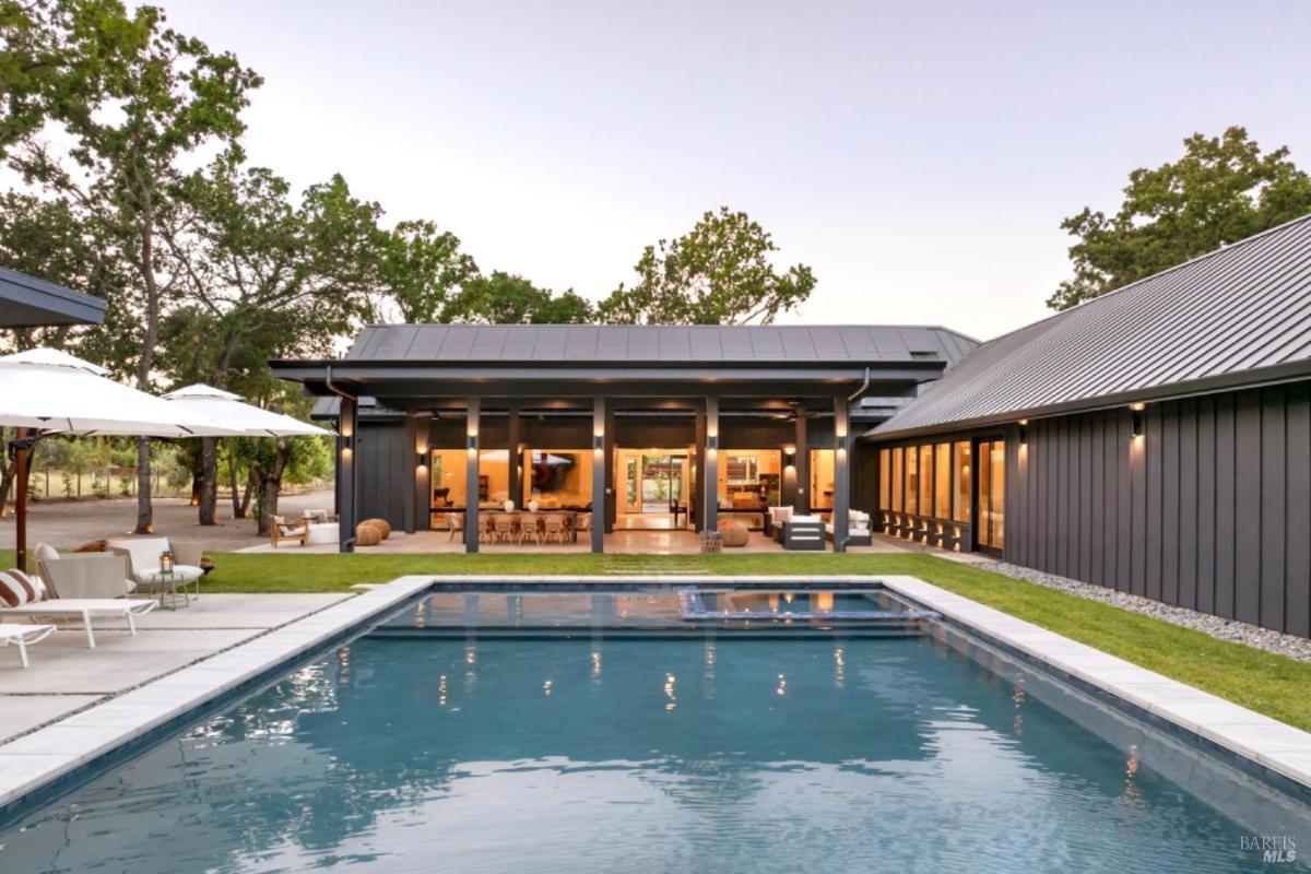 A modern house with an outdoor pool, lounge seating, and large glass doors leading to the interior.