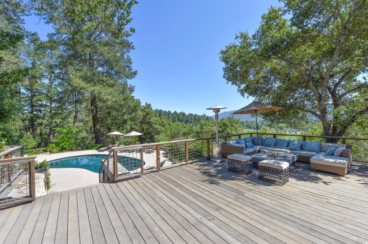 Deck with outdoor seating, overlooking a pool and greenery.