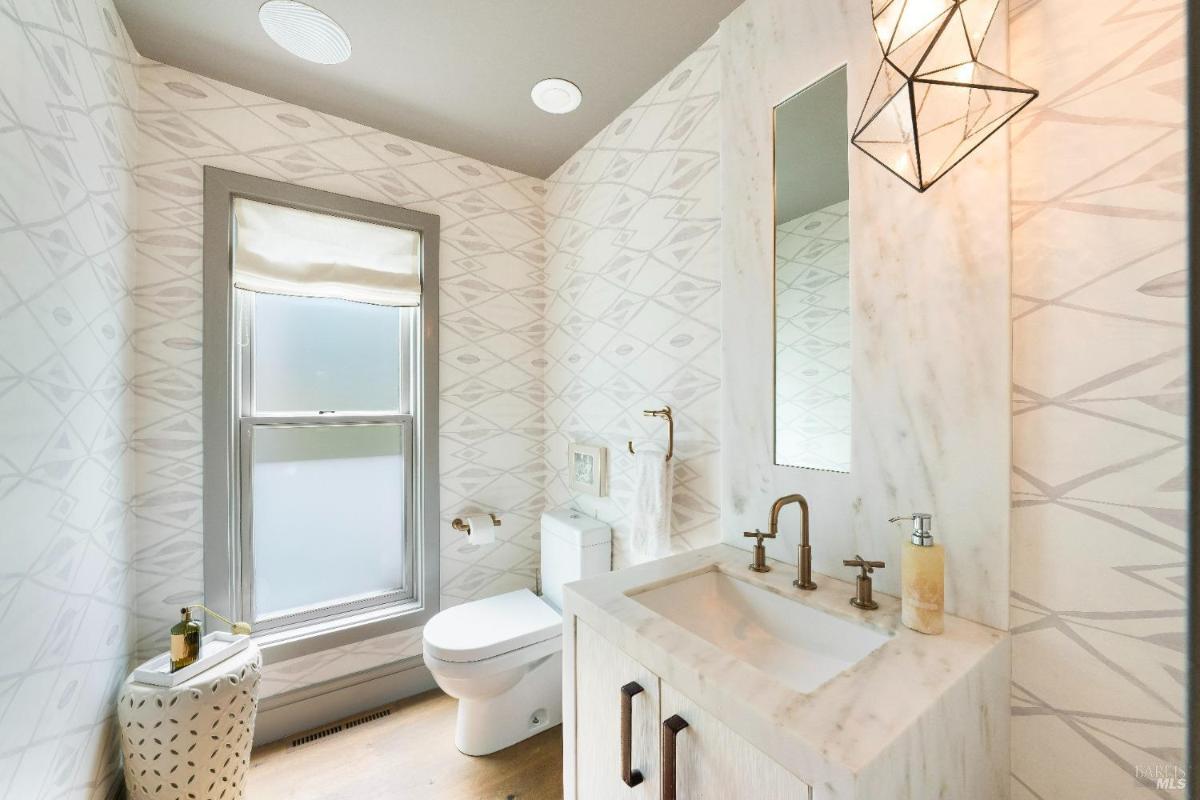 A compact bathroom with a single sink vanity, patterned walls, and a frosted window.