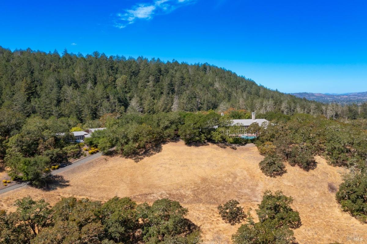 Aerial view of the house surrounded by forest and open dry grassland.