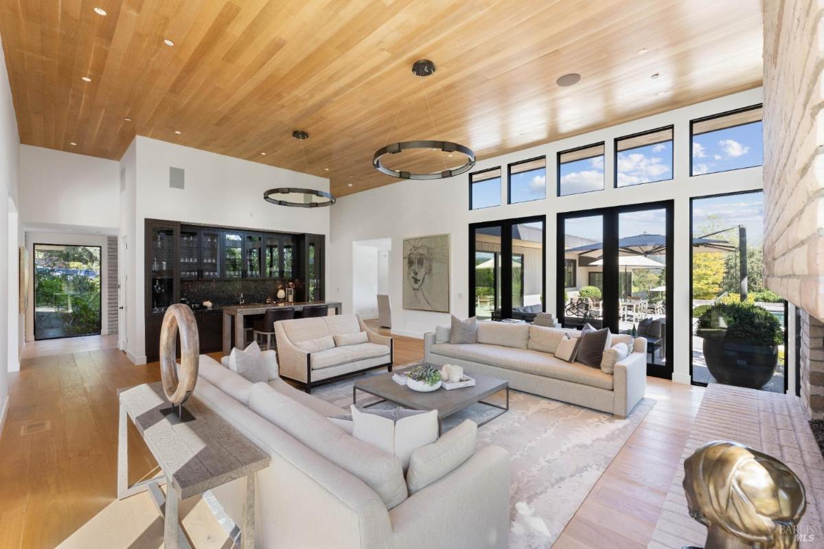 Living room with high ceilings, a wood-paneled ceiling, large windows, a fireplace, and seating arrangements.