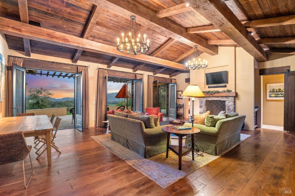 Living room with exposed wooden beams, chandeliers, and a view of the outdoor patio.