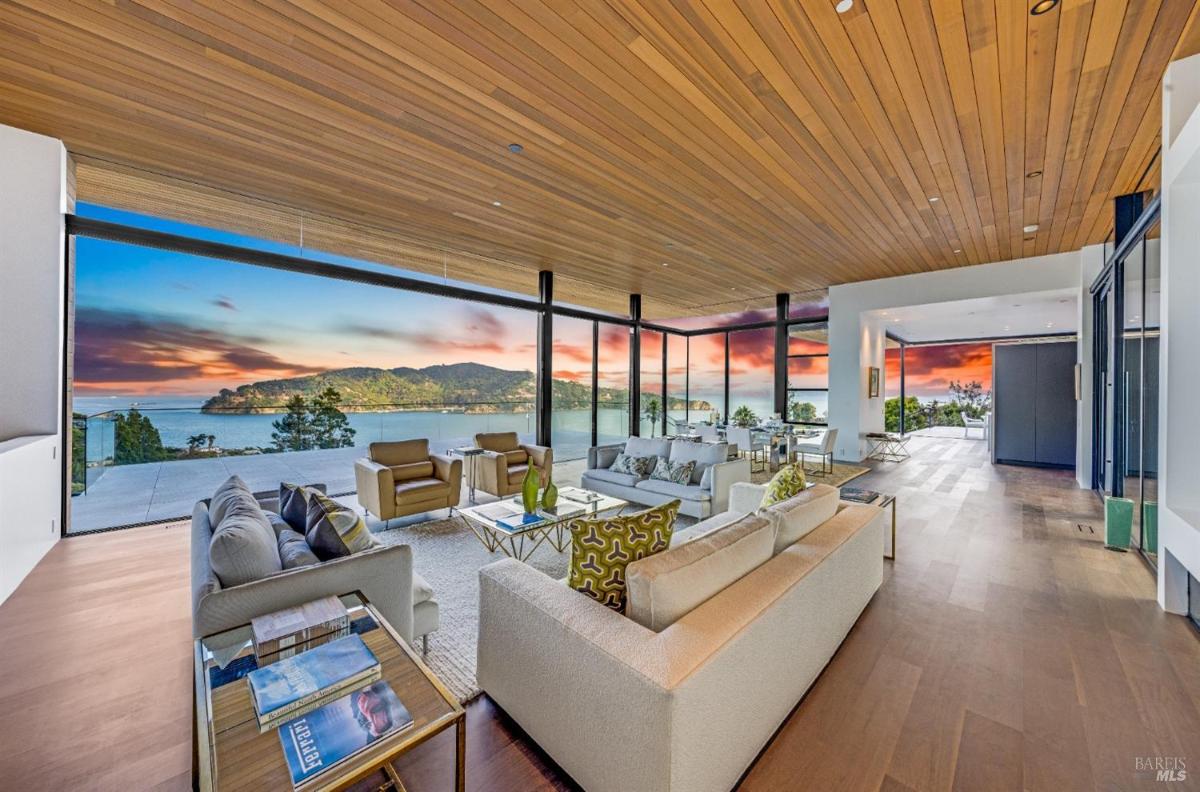 A large living area with floor-to-ceiling glass walls, contemporary seating, and a view at sunset.