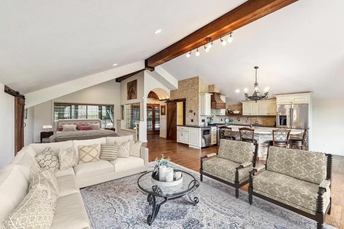 Combined living, kitchen, and bedroom area with visible beams and hardwood floors.