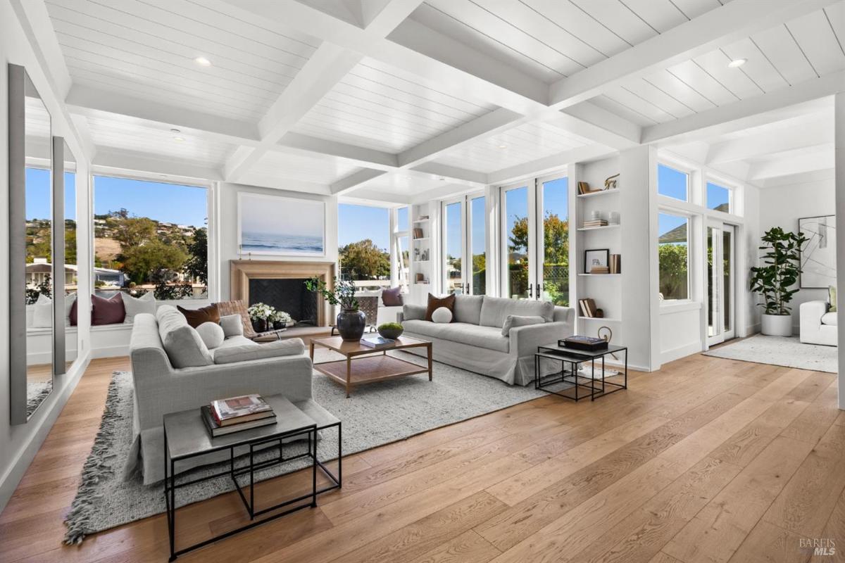 A living room with white sofas, a fireplace, and large windows overlooking the outdoors.