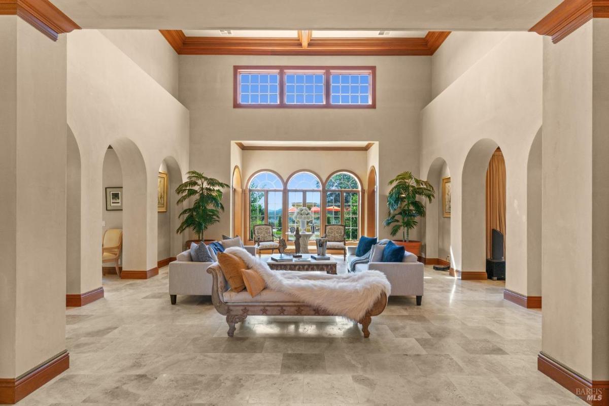 Living room with tall ceilings, archways, and expansive windows offering garden views.