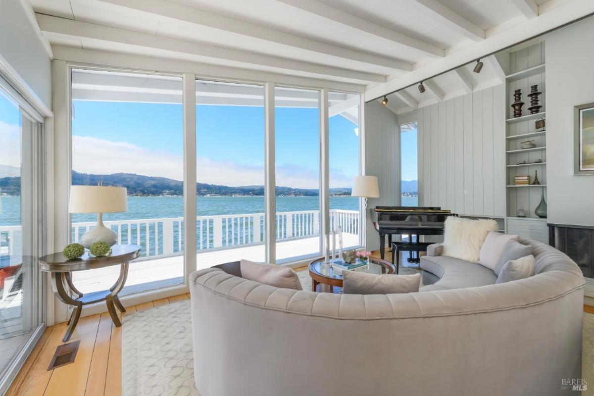 Lounge area with curved couch, piano, and floor-to-ceiling windows overlooking the water.