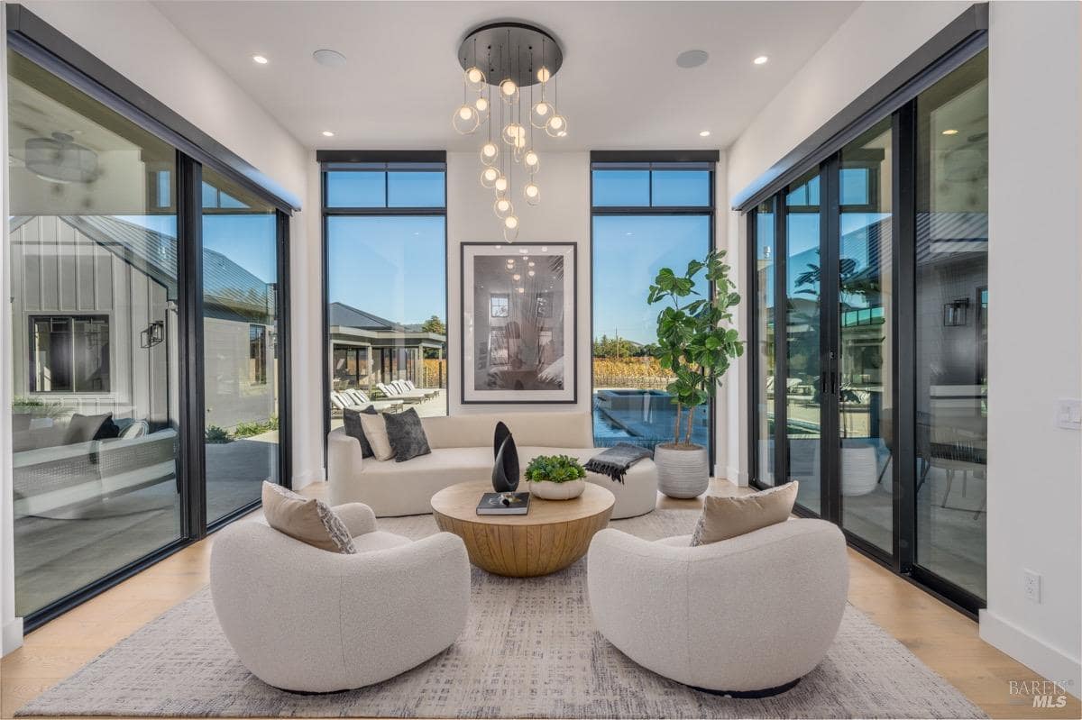 Living room with floor-to-ceiling windows, round coffee table, white seating, and a central light fixture.