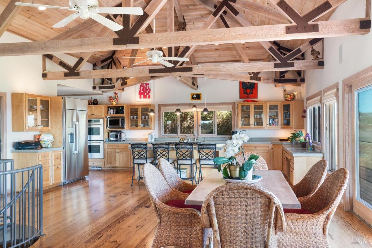 Dining area with wicker chairs, a wood table, and glass doors leading to a balcony overlooking vineyards.