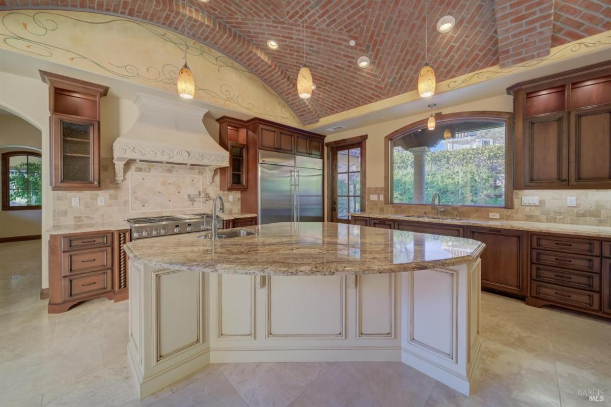 A kitchen featuring a large island, brick arches, and wooden cabinetry.