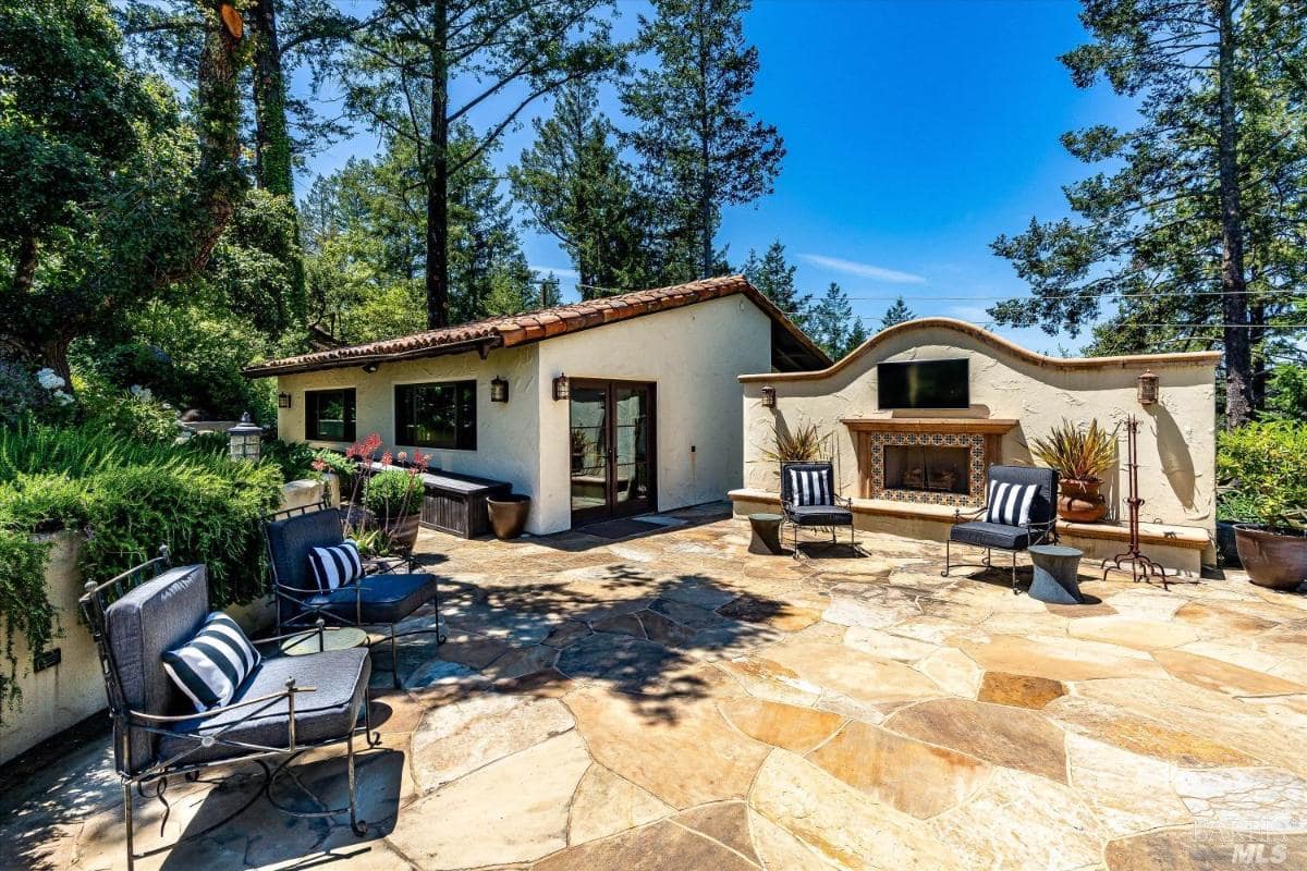 A patio with an outdoor fireplace, chairs, and access to a guesthouse.