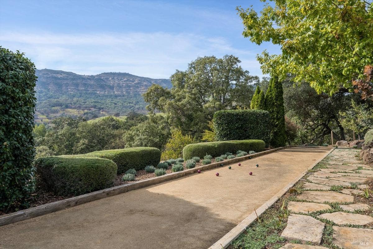 A bocce court bordered by trimmed hedges, with surrounding greenery and a mountain view.