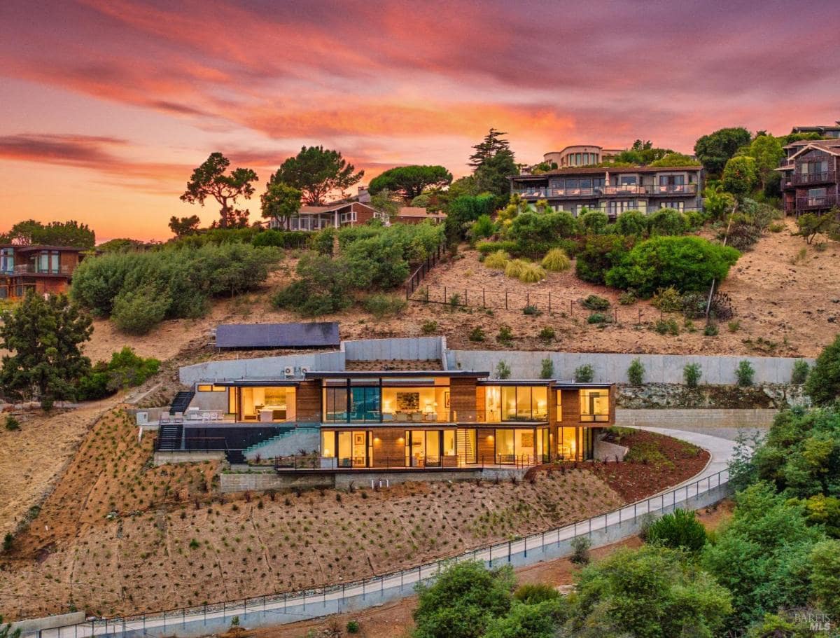 Thought about hillside home view for a second A multi-level modern house built into a hillside, with large windows and a sloping driveway.