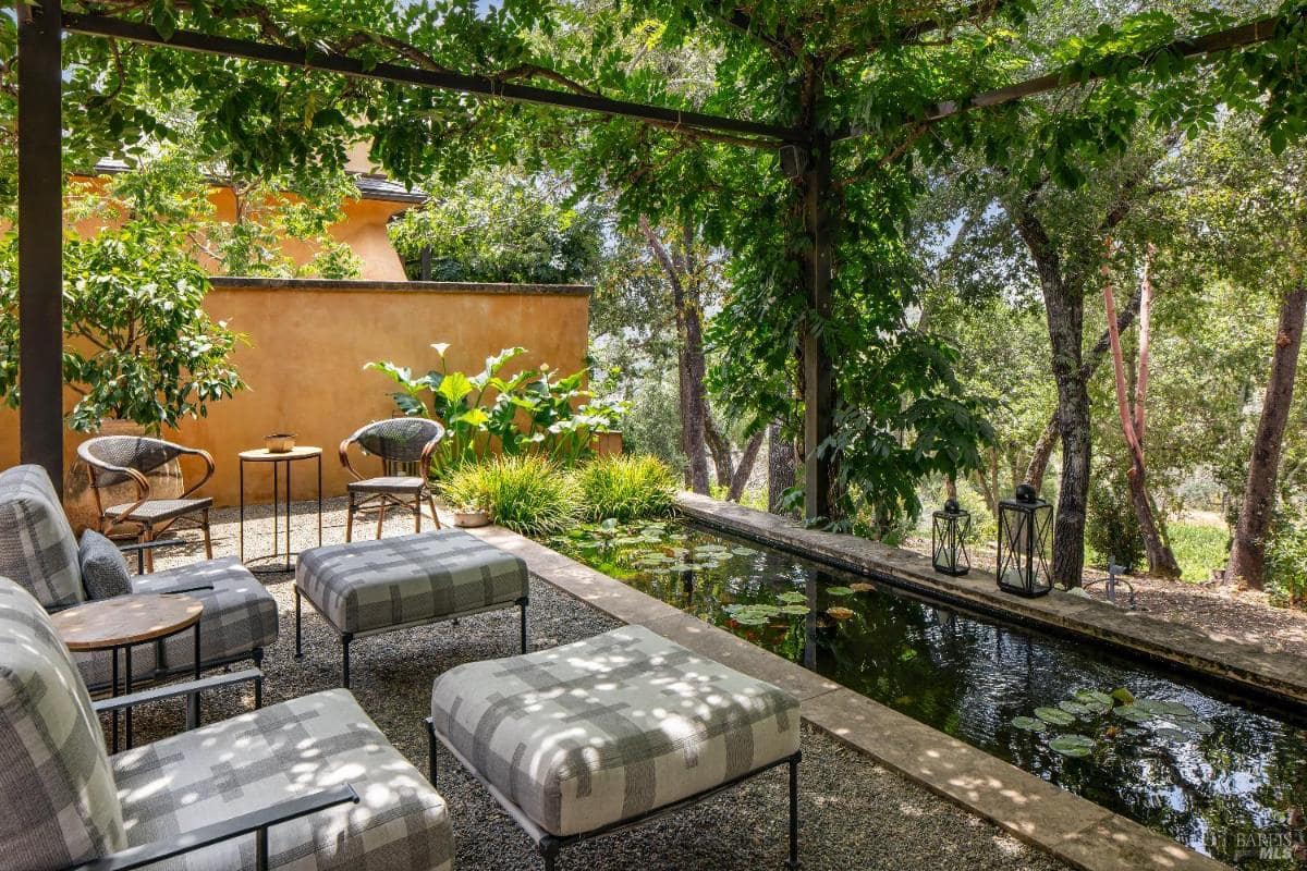 A garden seating area with chairs and a pond surrounded by greenery.