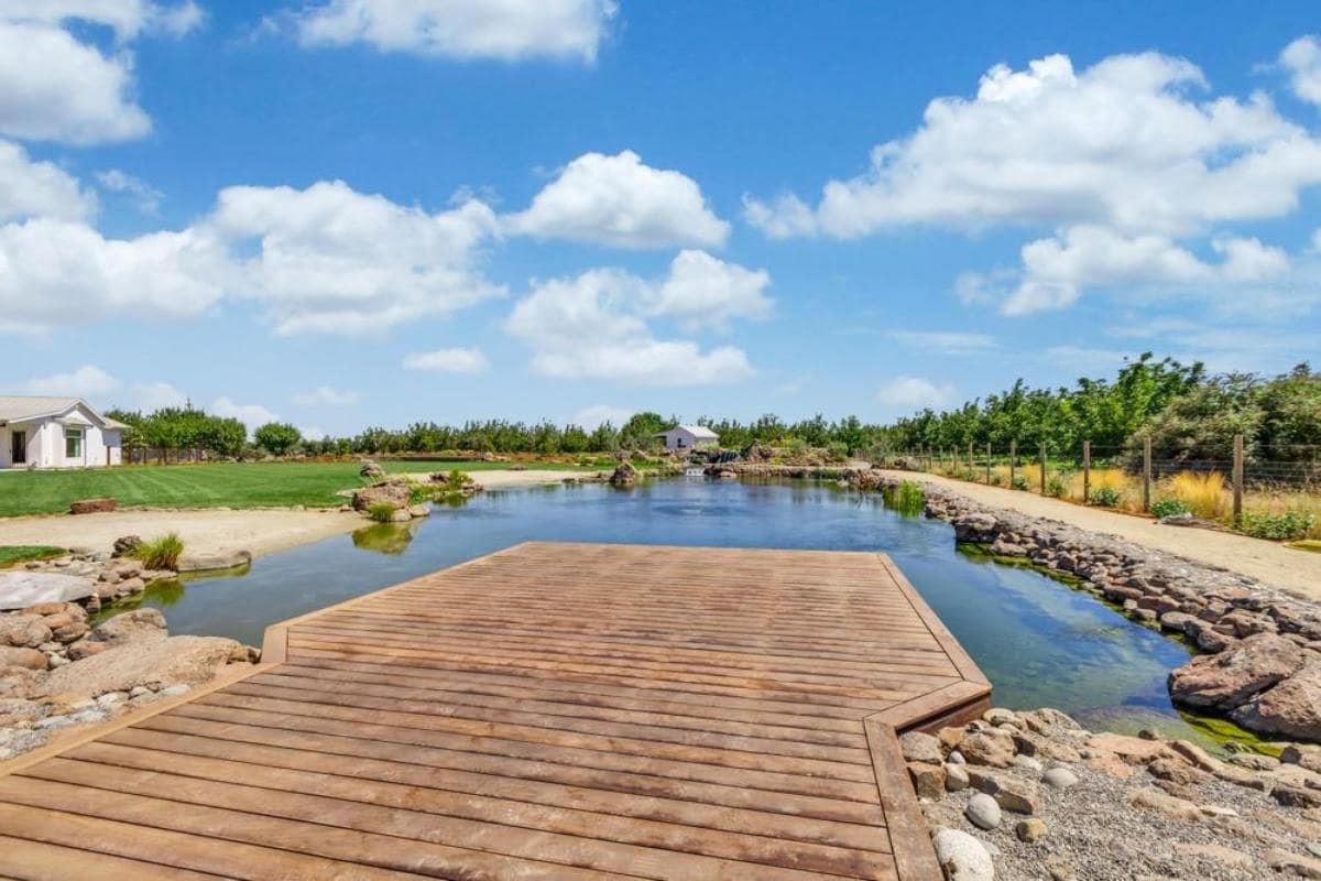 Wooden dock extending into a calm body of water surrounded by grass and trees.