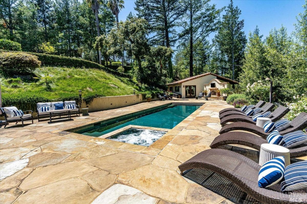 A pool area with a spa, lounge chairs, and a patio surrounded by greenery.