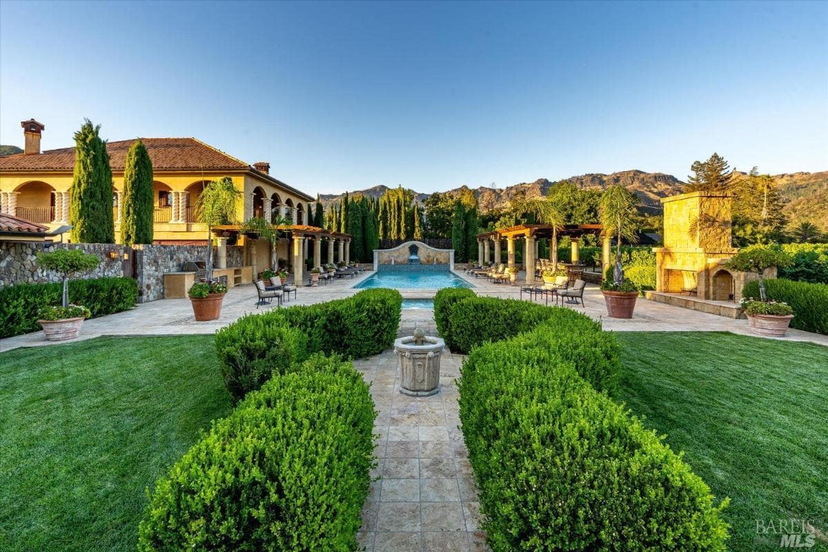 A view of a mansion with a vineyard in the background.