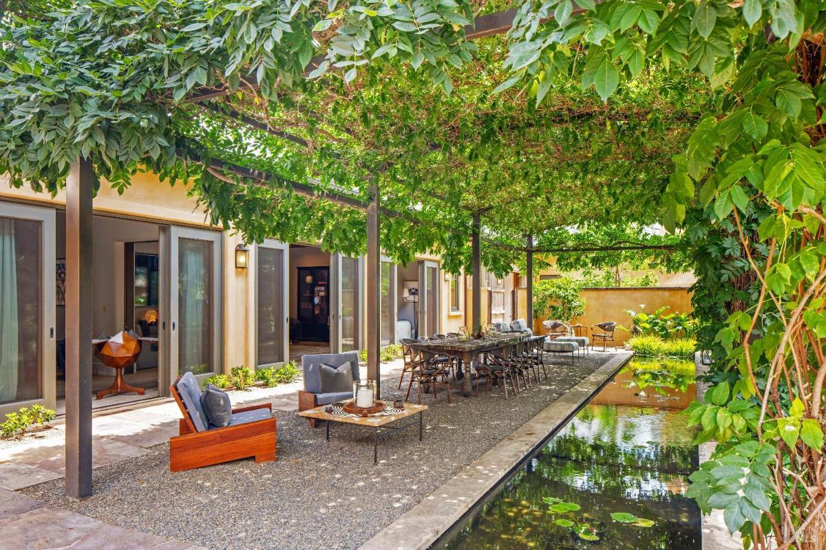 Outdoor seating and dining area under a pergola with a reflecting pond nearby.