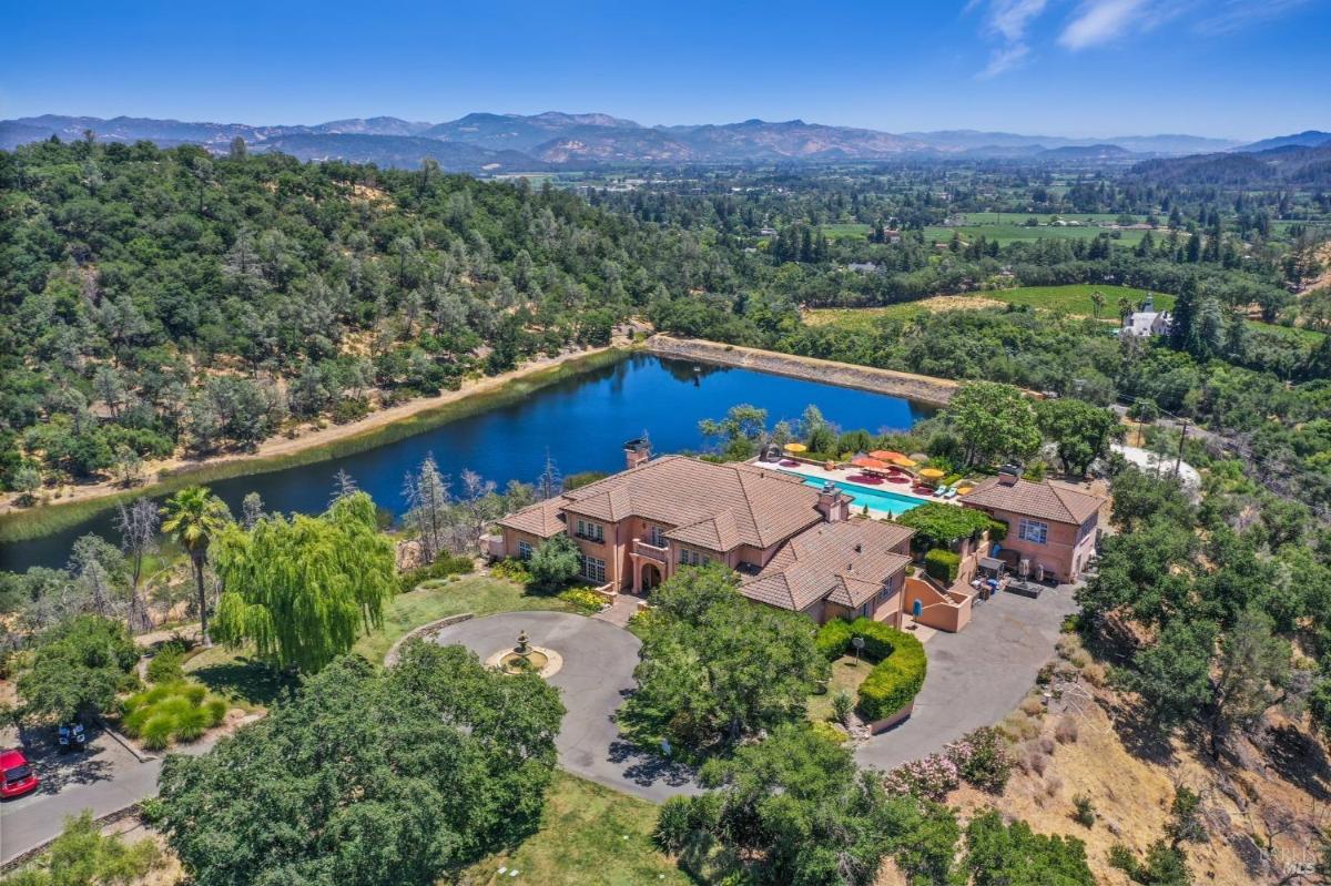 A view of the home and its surrounding landscape, featuring a private lake and lush wooded areas. 