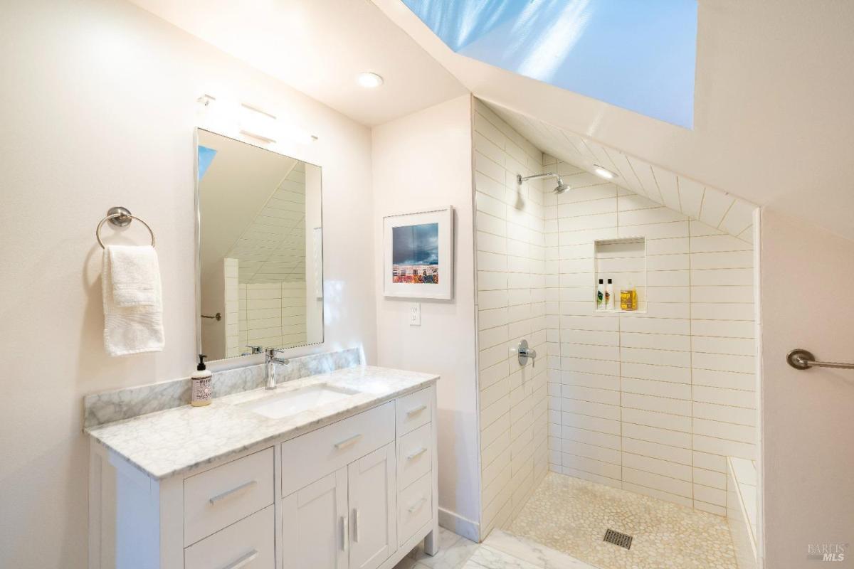 A bathroom featuring a marble vanity, walk-in shower, and skylight.