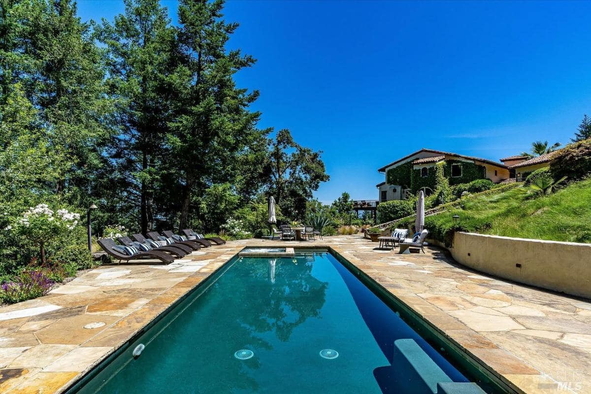 A swimming pool lined with lounge chairs and a view of the house and landscaping.