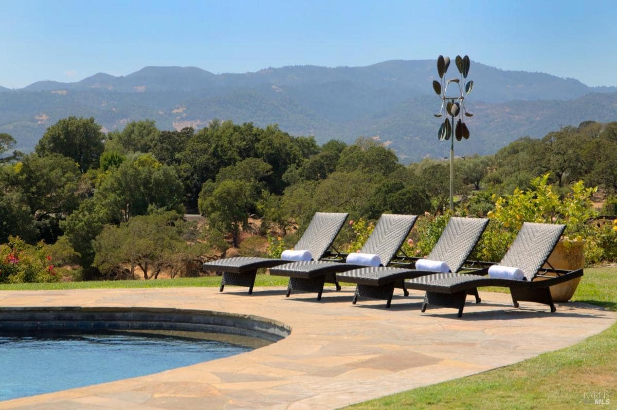 A pool area with lounge chairs and a view of the mountains.