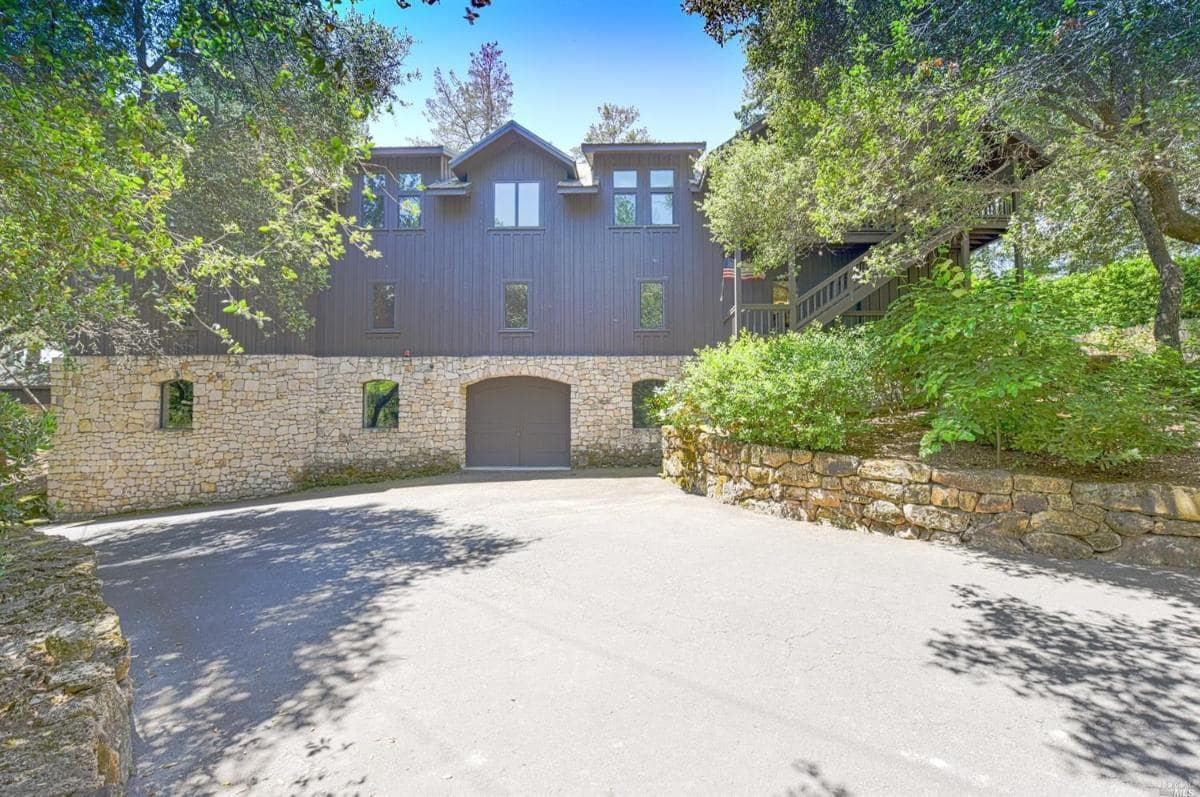 Building exterior with stone base and dark wood siding, surrounded by trees.