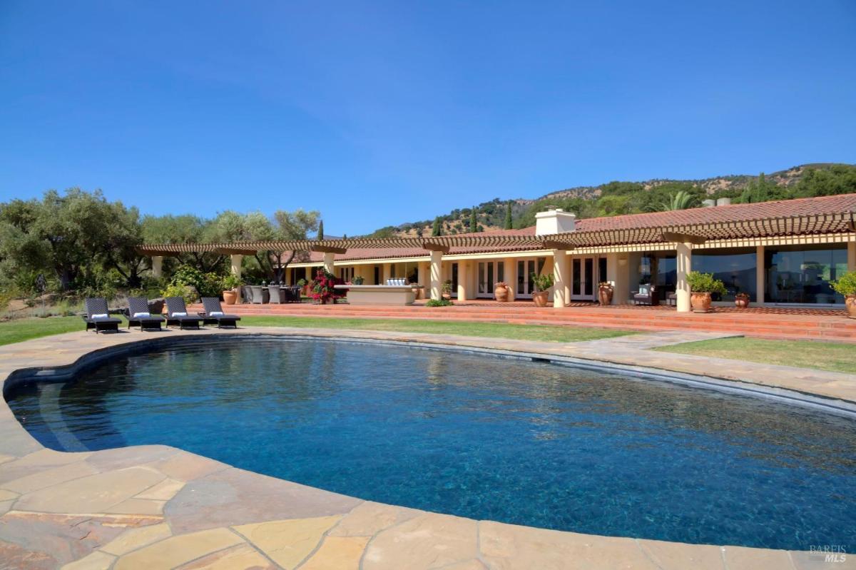 A large pool with a terracotta-tiled patio and a single-story home in the background.