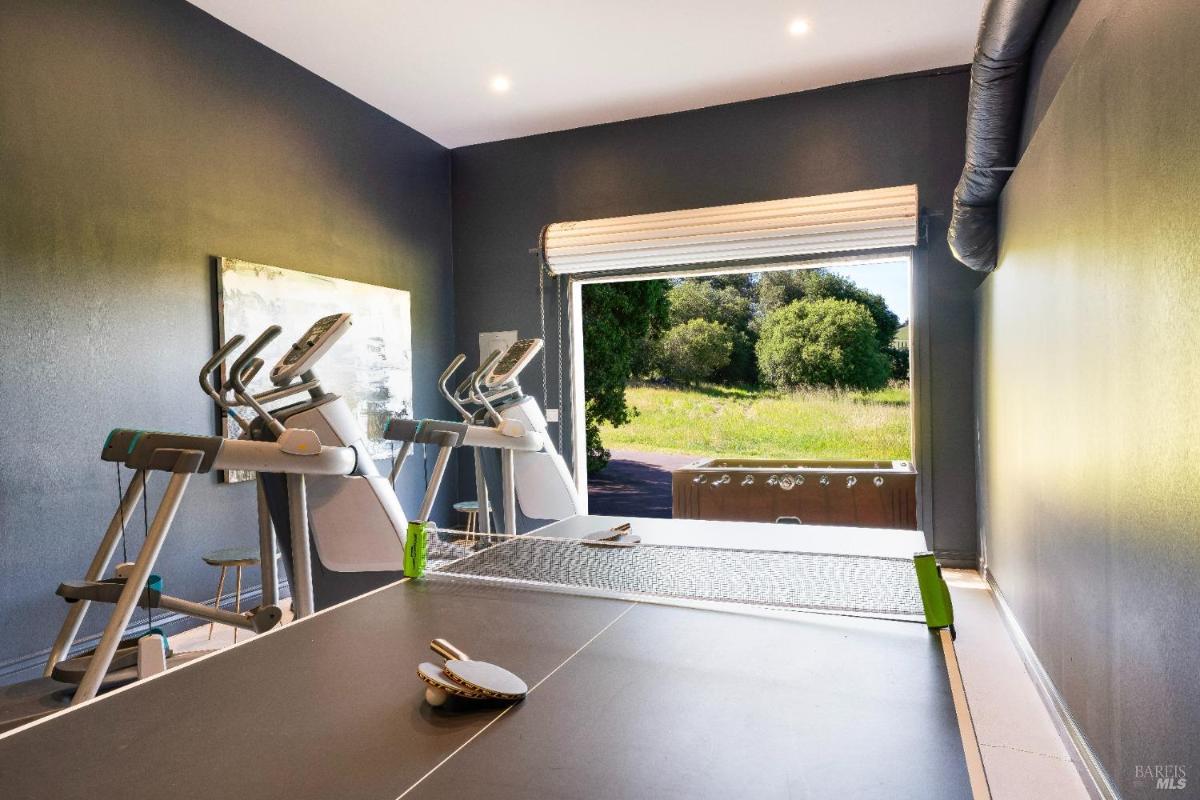 A home gym with treadmills and a ping pong table, open to a green outdoor space.