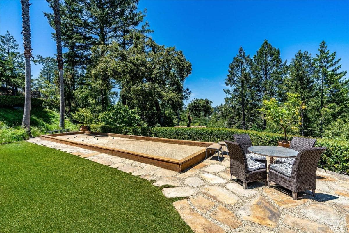 A bocce court and a seating area on a stone patio surrounded by trees.