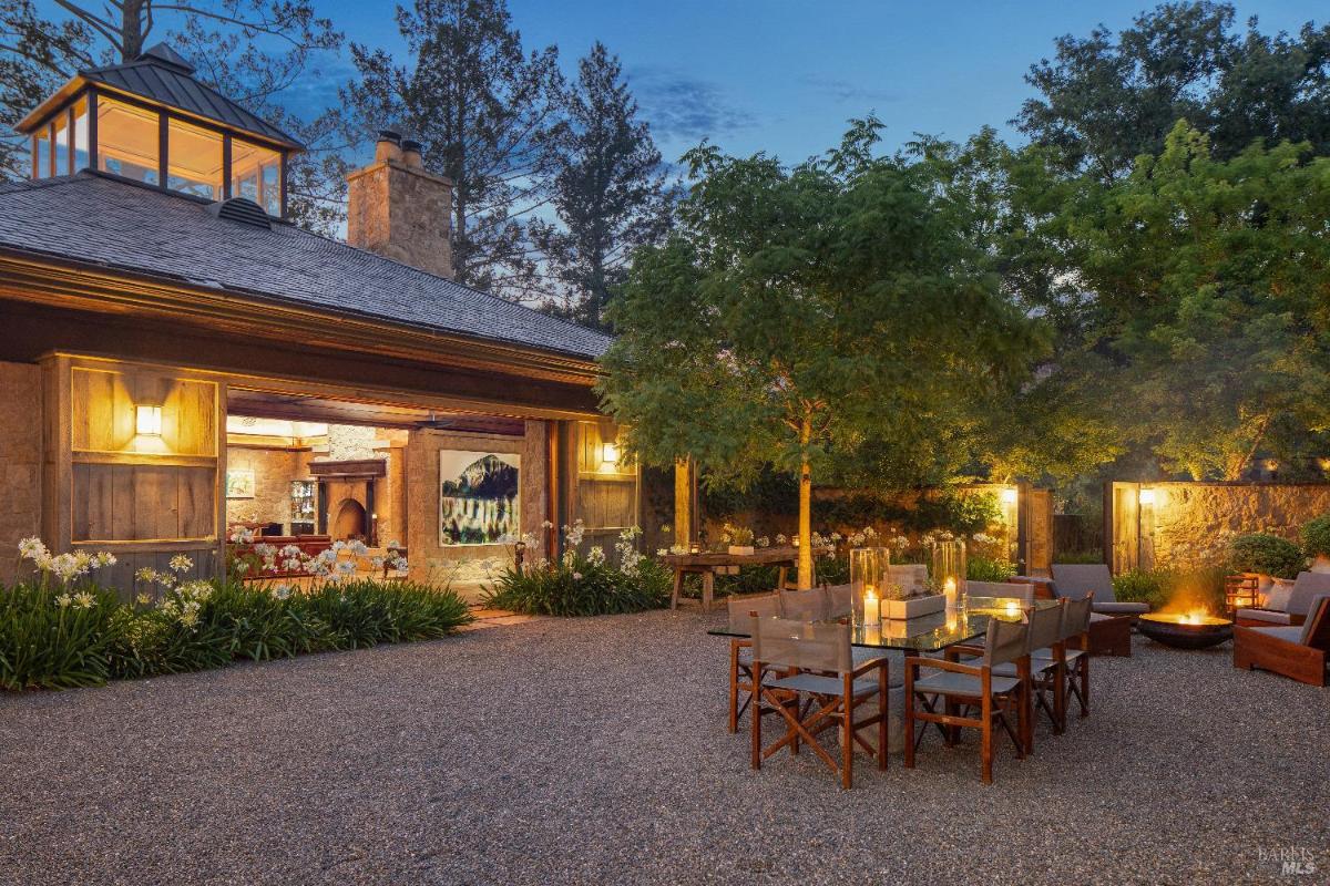 Outdoor courtyard with a dining table, seating, and fire pit illuminated at dusk.