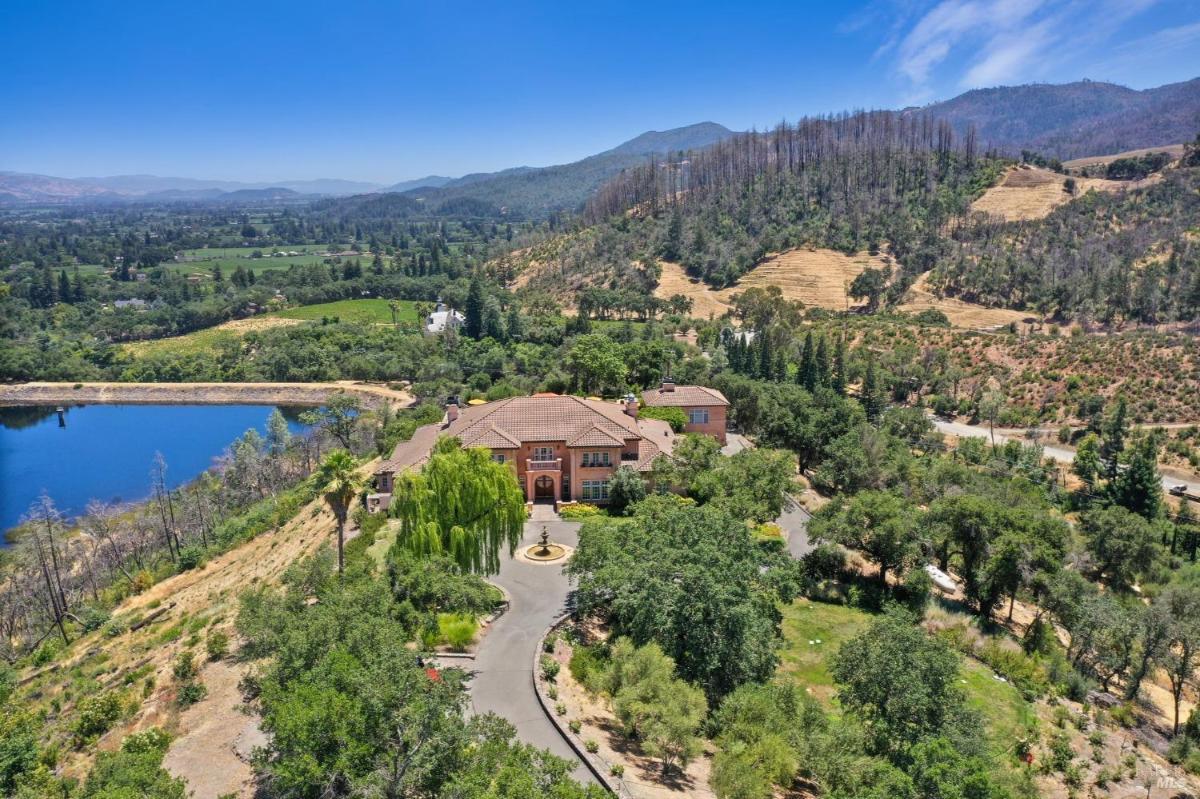 A house nestled in a scenic valley surrounded by forested hills and vineyards. 