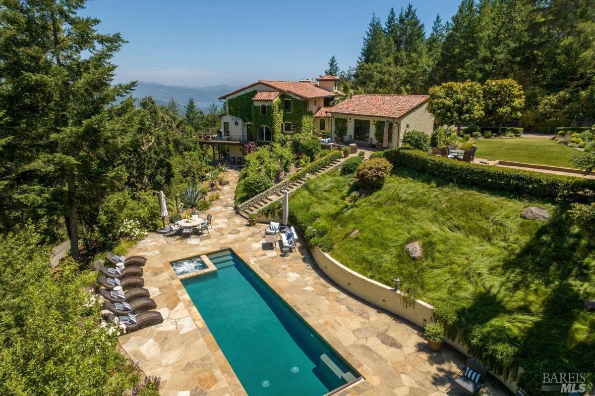 A house and pool surrounded by greenery, with a view of landscaping and terraces.