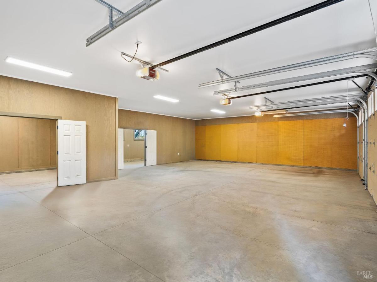 Garage interior with multiple doors, concrete flooring, and overhead lighting.