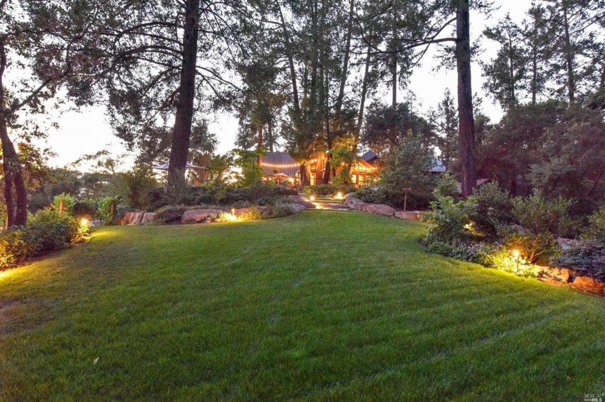 A lawn with a view of a house illuminated at dusk.