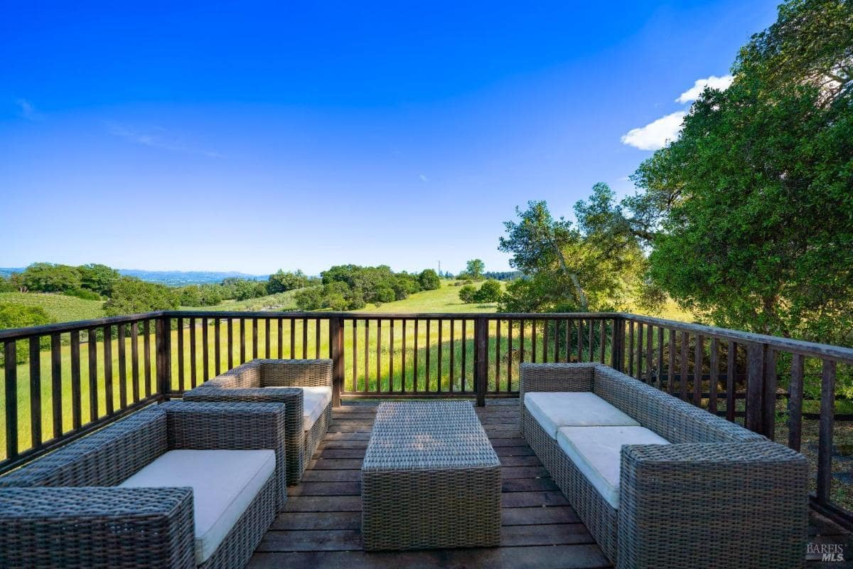 A deck with seating and a coffee table overlooking a grassy landscape. 