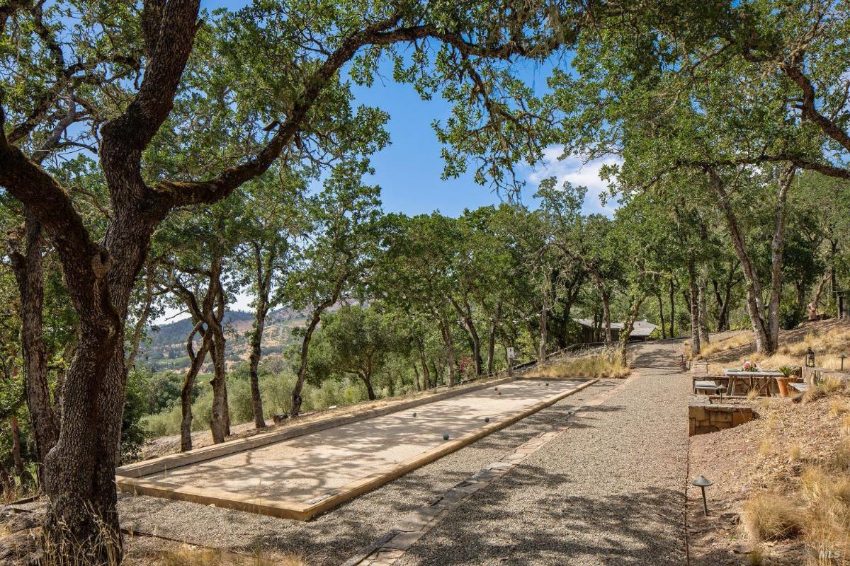 Gravel path lined with trees and a bocce ball court in a forested area.