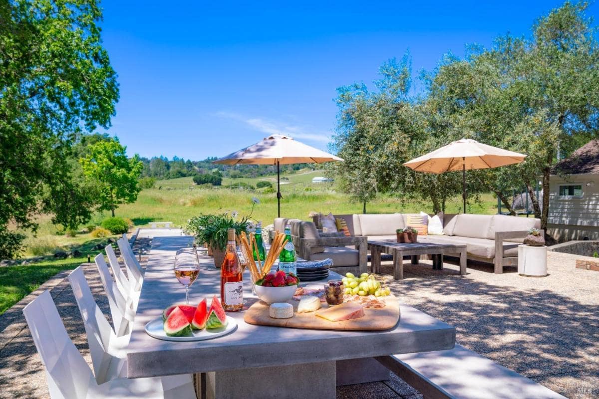 A patio area features a table with food and drinks surrounded by outdoor seating and umbrellas. 