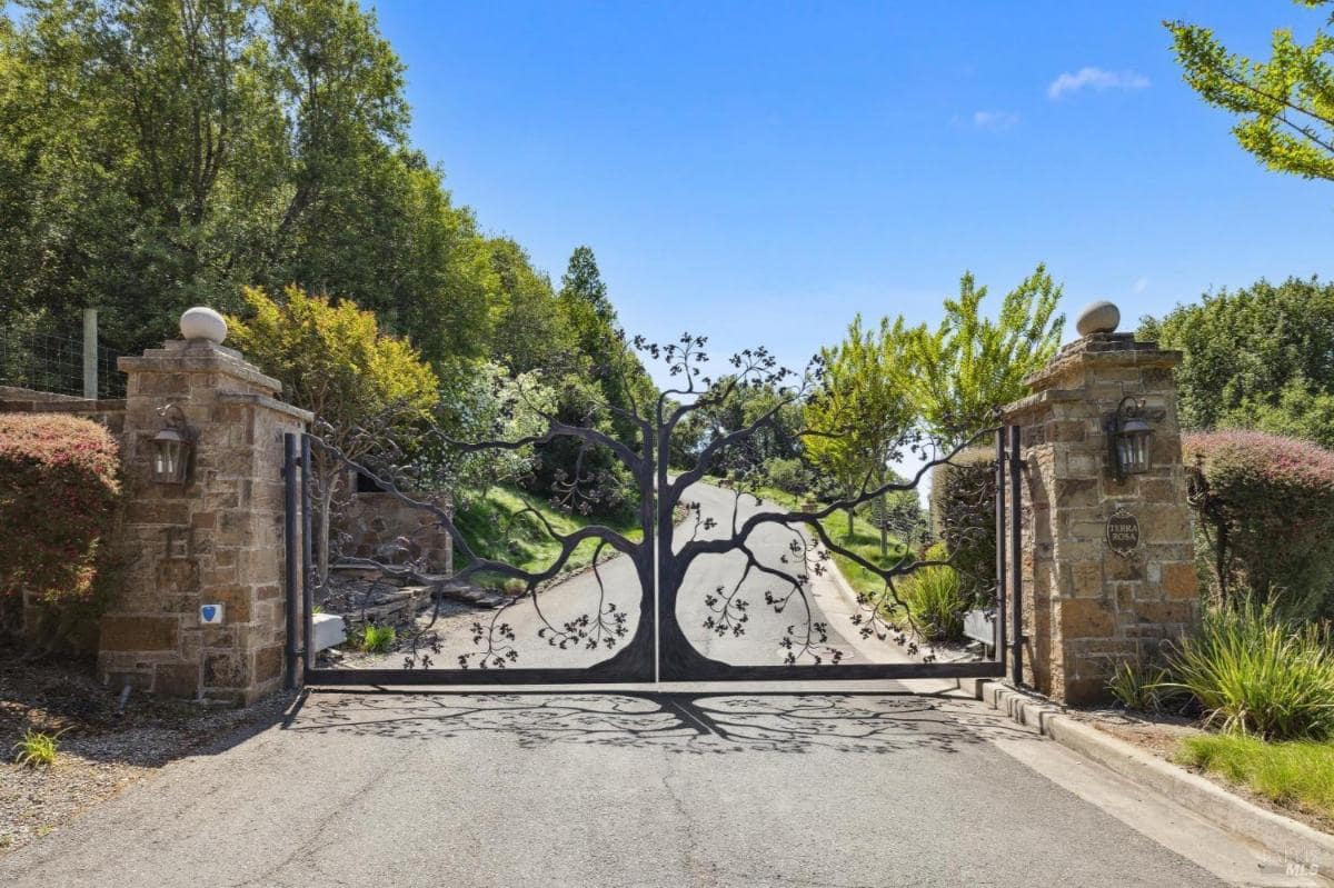 A decorative wrought iron gate shaped like a tree, set between stone pillars.