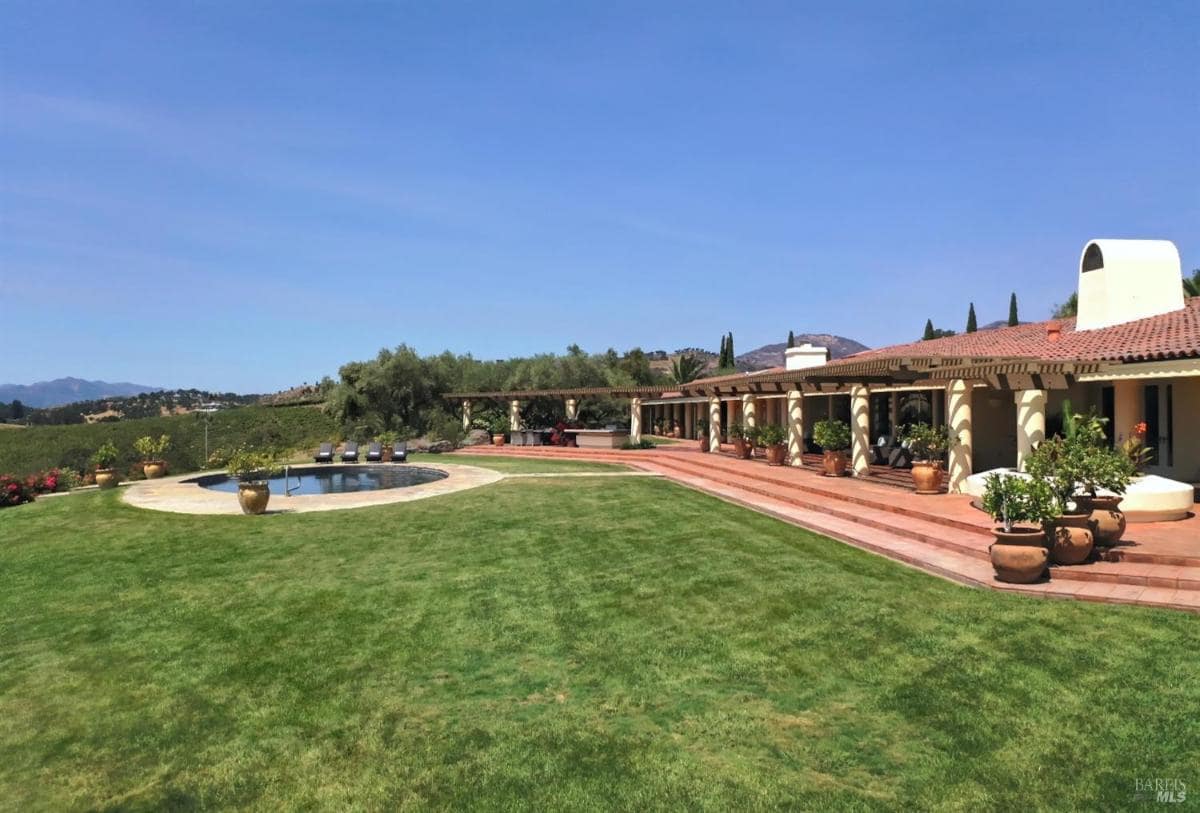 Expansive lawn with a pool and a single-story house featuring a tiled roof in the background.