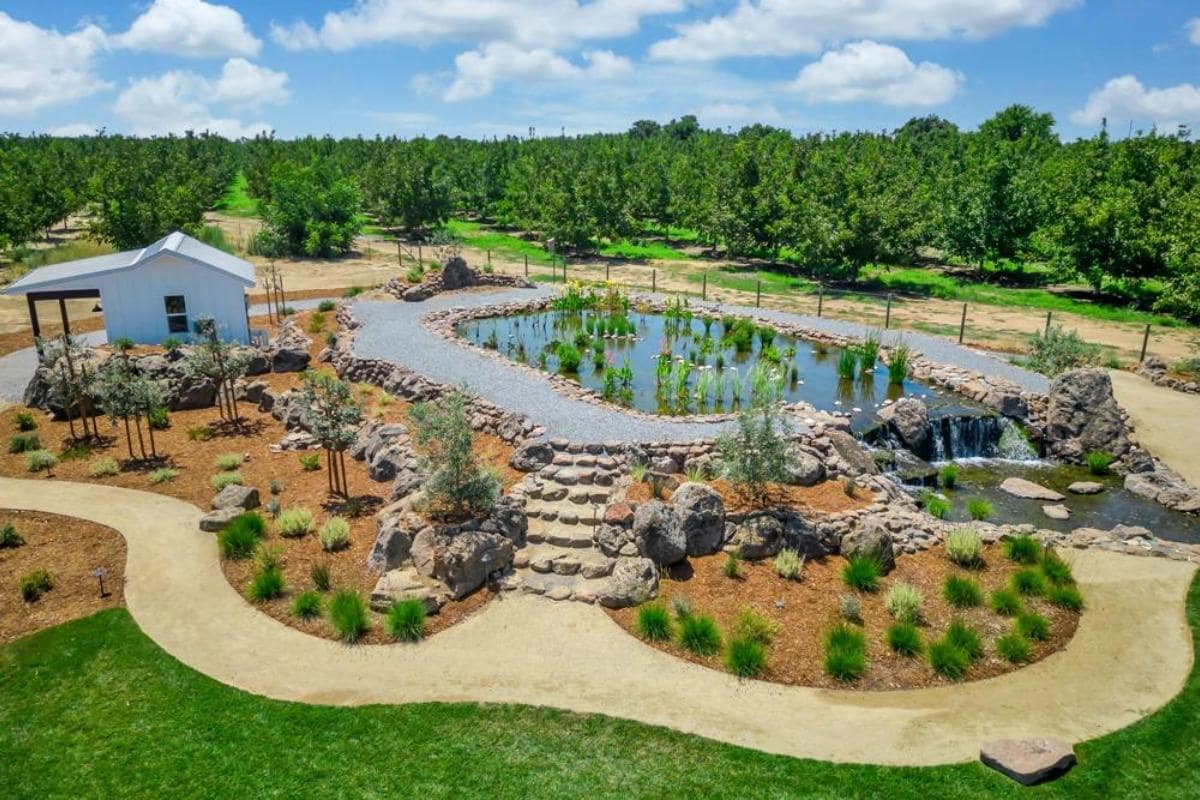 Aerial view of a landscaped garden featuring a pond, rocks, and pathways, surrounded by trees.