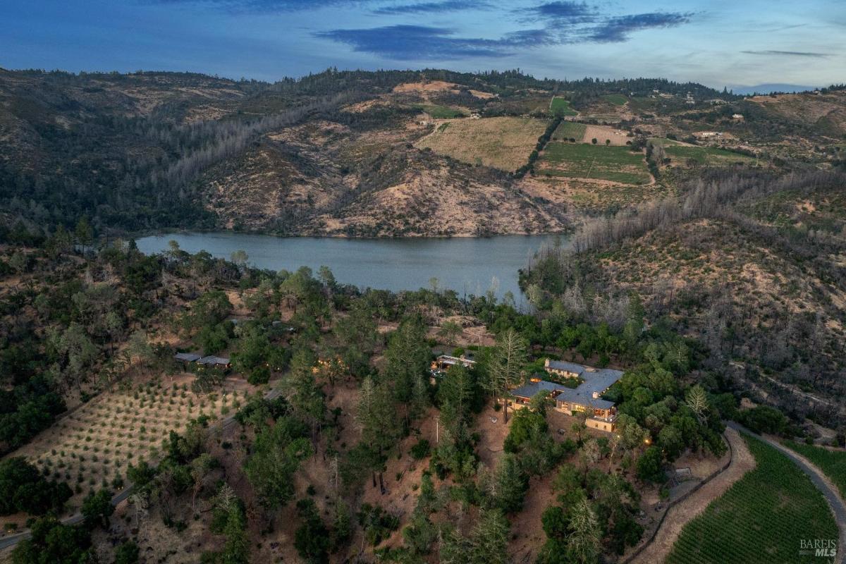 Aerial view of a house near a lake, surrounded by hills and open land.